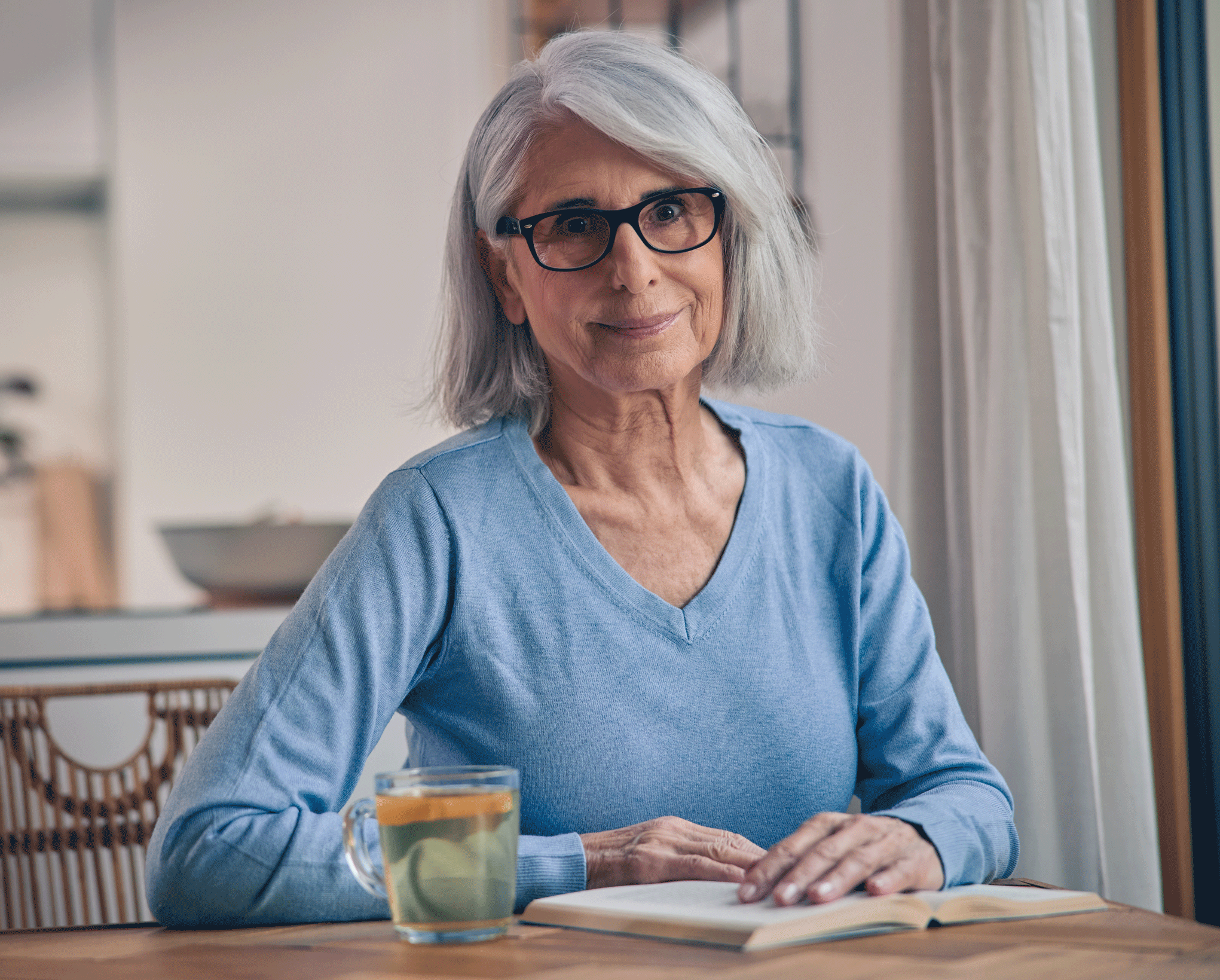 Frau mit Buch und Tee in der Küche: Viel trinken kann gegen eine Reizblase helfen.