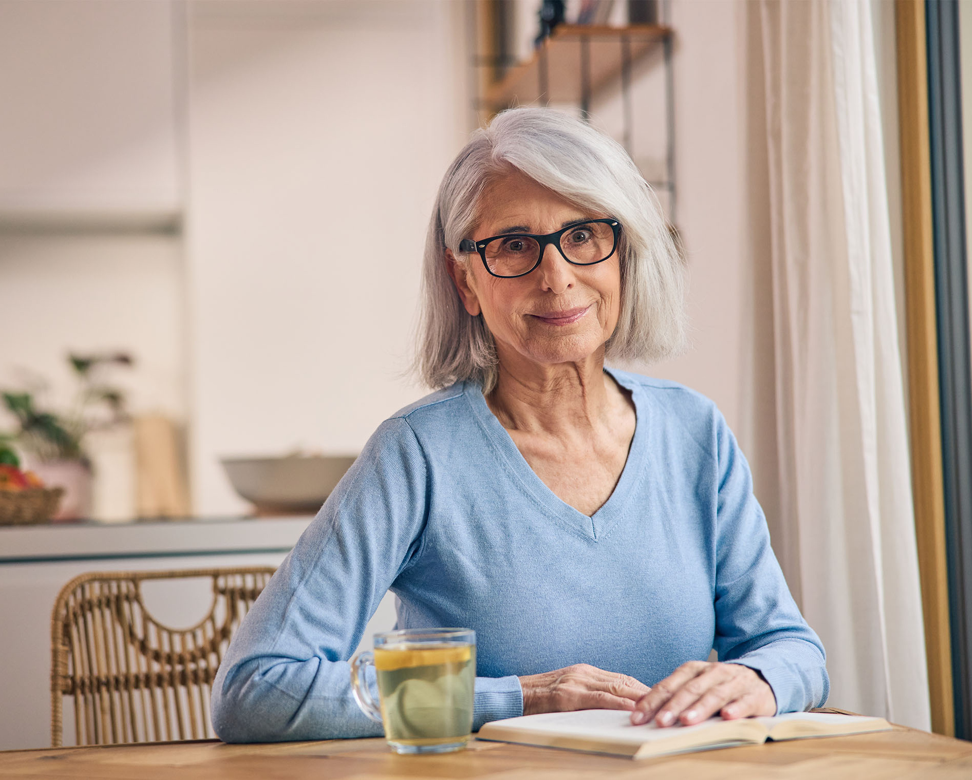 Frau mit Buch und Tee in der Küche: Viel trinken kann gegen eine Reizblase helfen.