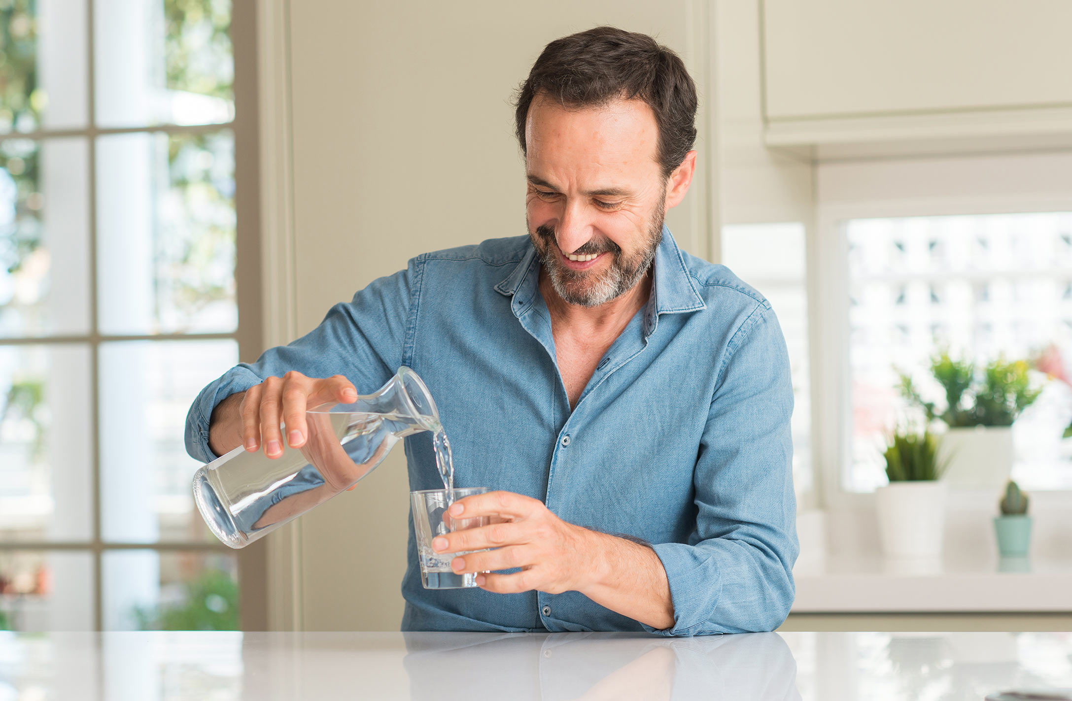 Mann schenkt sich für die Anwendung von UROL FLUX® ein Glas Wasser ein.